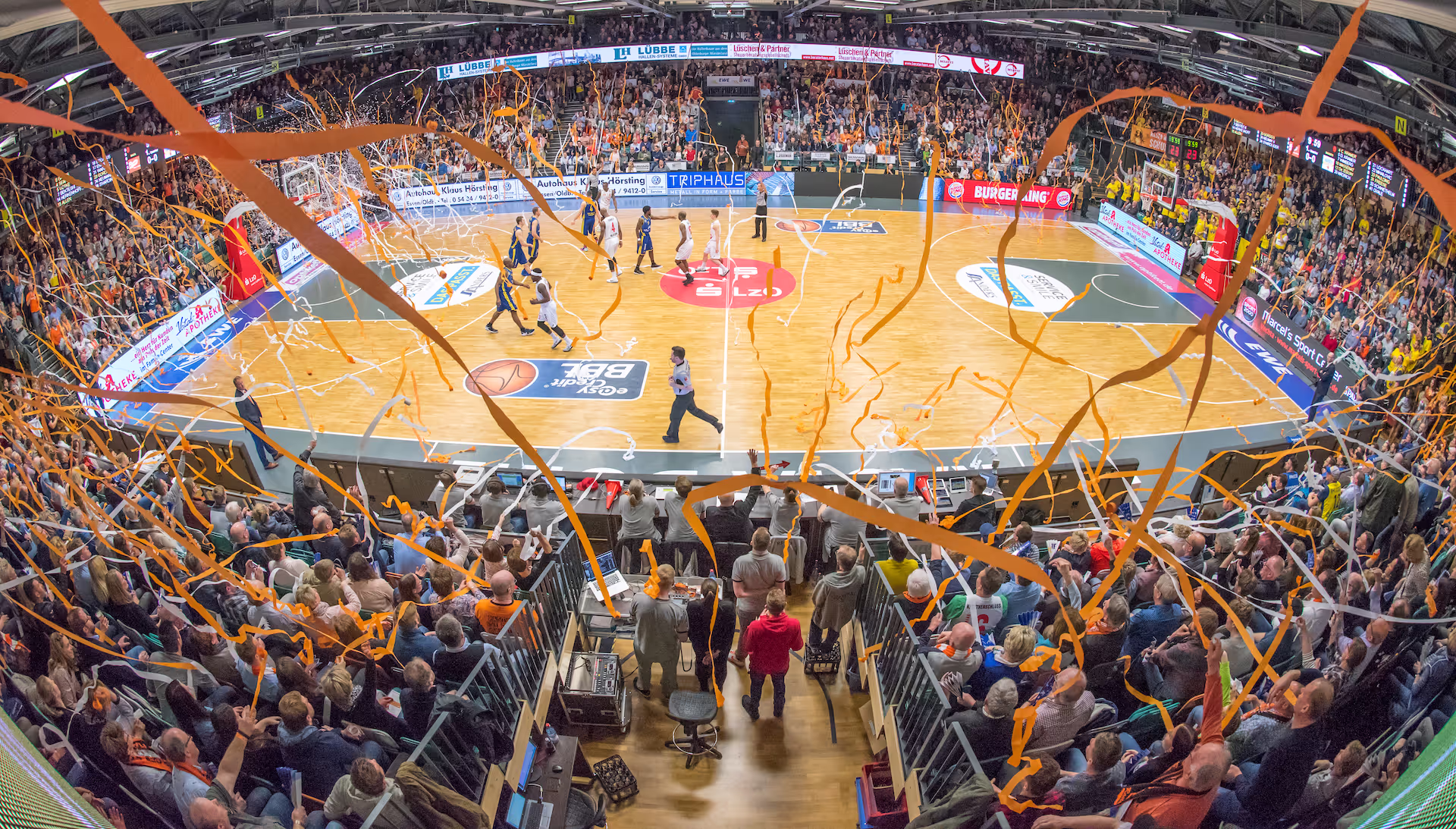 Panoramablick in den RASTA Dome: orangefarbene Luftschlangen über dem Spielfeld und voll besetzte Ränge