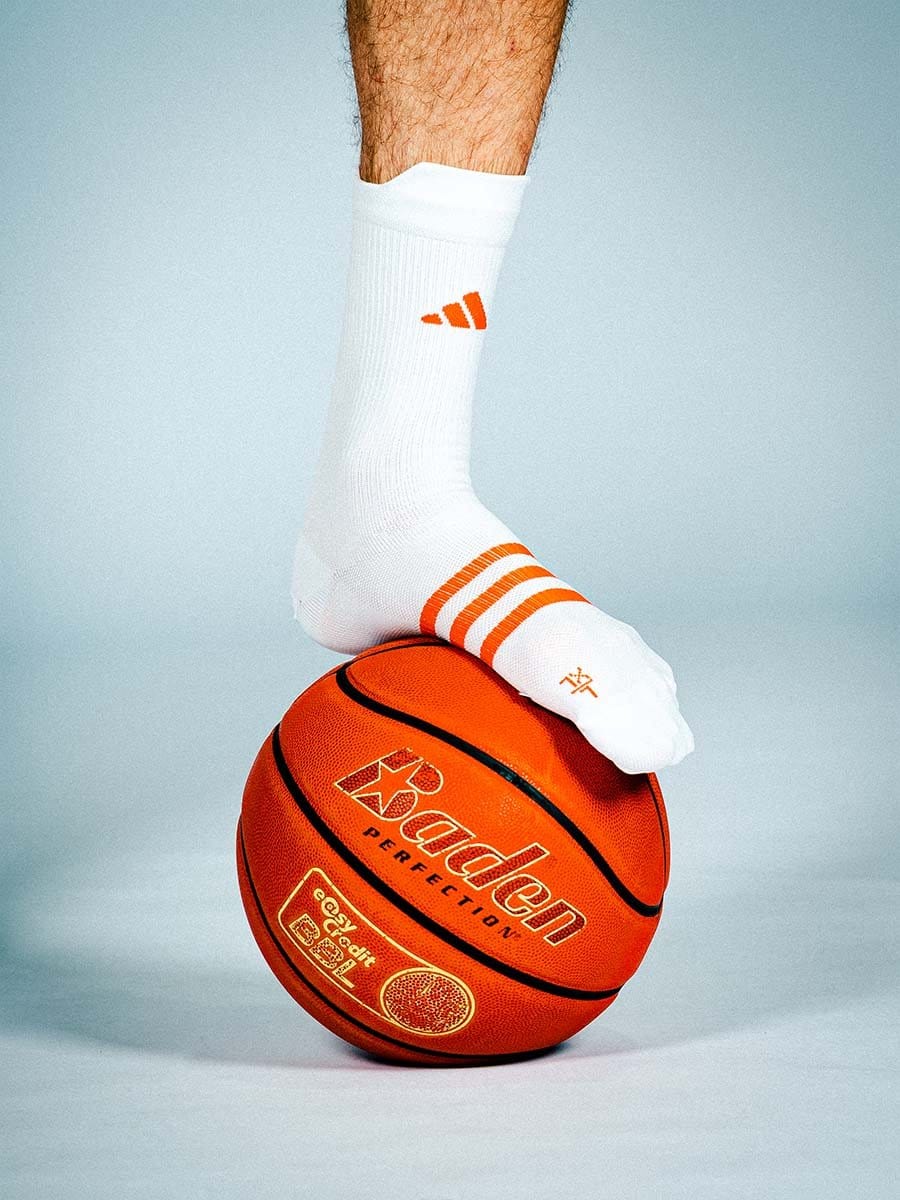 Ein Bein mit weißem Sportsocken, die orange Streifen und Logos haben, steht auf einem orangefarbenen Basketball.