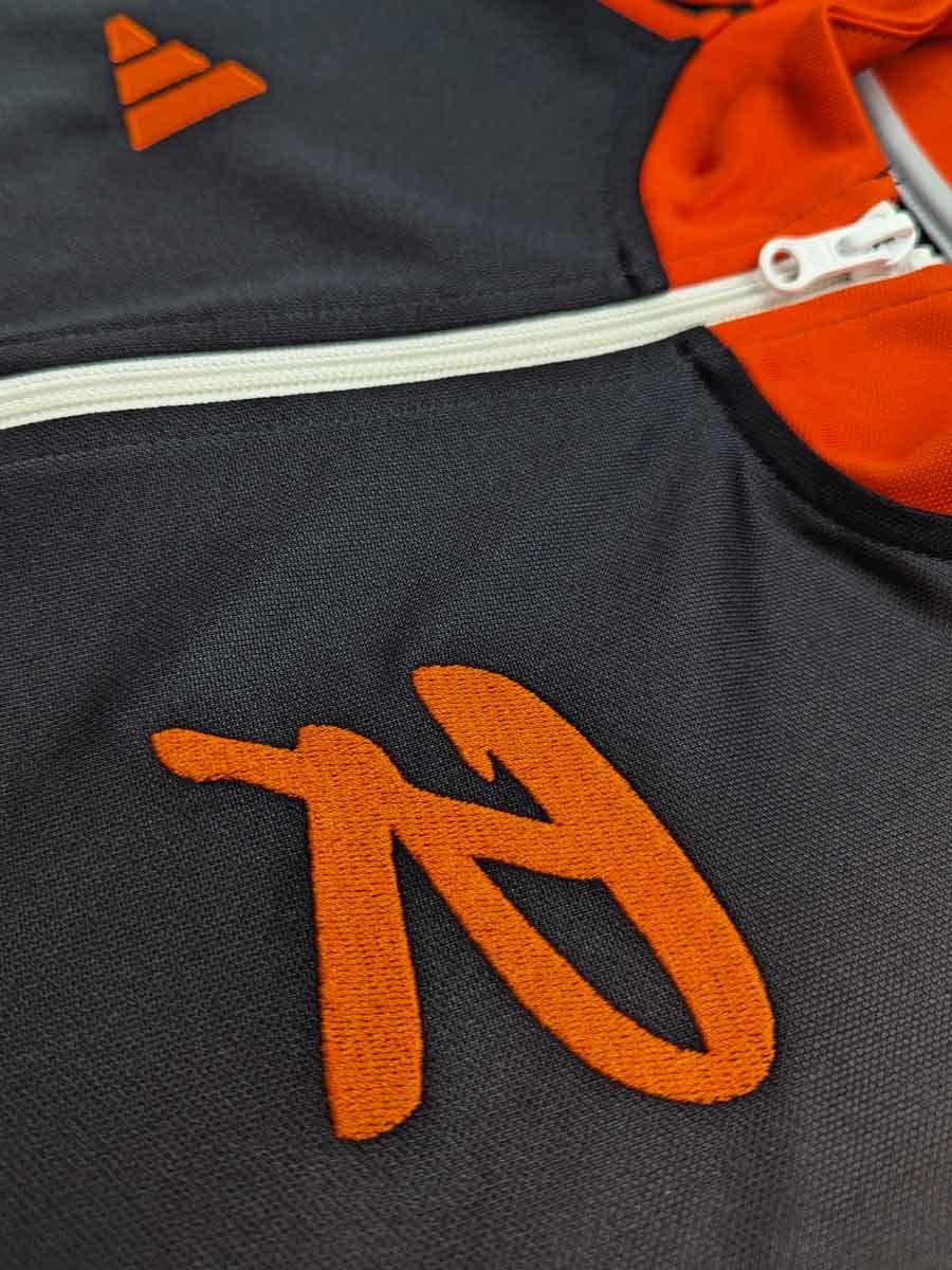 Nahaufnahme eines schwarzen Rucksacks mit orangefarbenem Logo und einer weißen Reißverschluss.