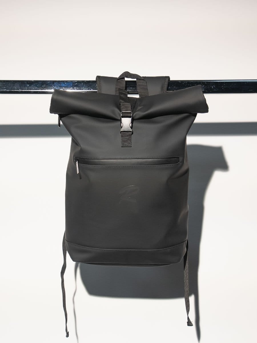 Schwarzer Rucksack aus wasserabweisendem Material, hängt an einer schwarzen Stange, mit verstellbaren Schultergurten und einer vorderen Reißverschlusstasche.