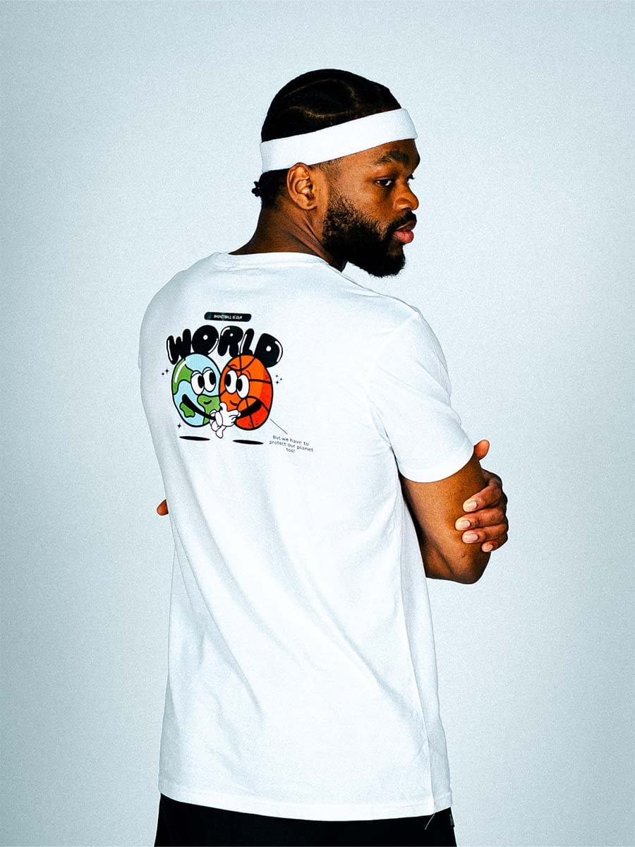 Mann trägt weiße T-Shirt mit buntem Cartoon-Design und Text, dazu weißen Stirnband, steht seitlich vor hellem Hintergrund, Arme verschränkt.