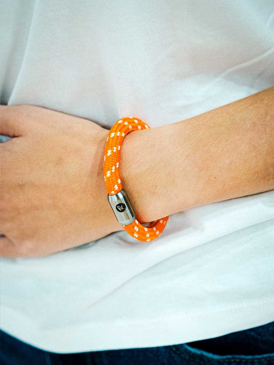 Armband aus orangefarbenem, reflektierendem Material mit weißen Punkten, mit silbernem Magnetverschluss am Handgelenk.