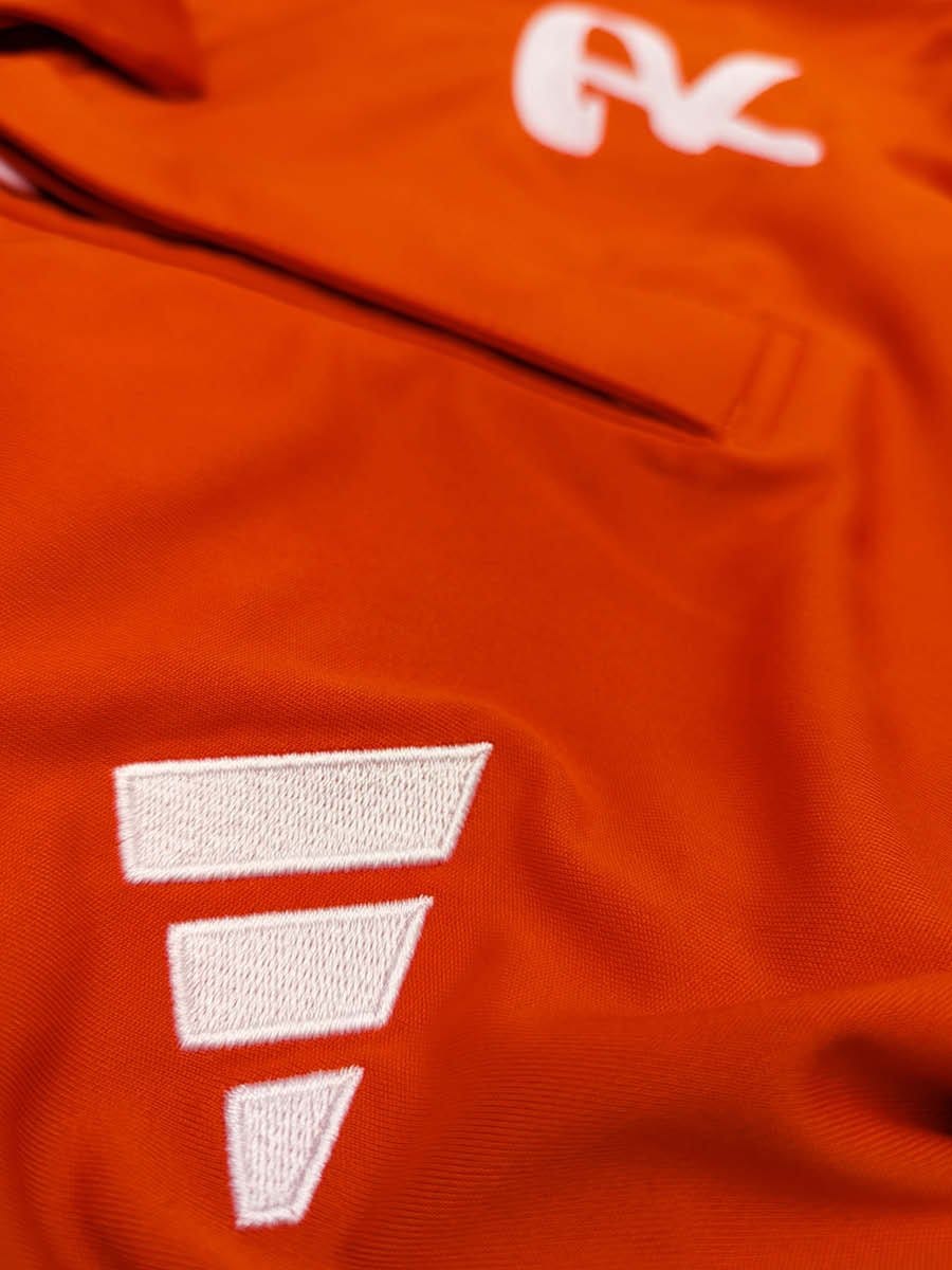 Nahaufnahme eines orangefarbenen Stoffes mit weißen, gestickten Buchstaben und einem Reißverschluss.