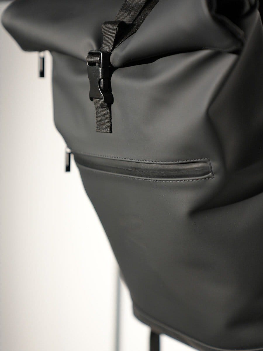 Schwarzer Rucksack mit rollbarem Verschluss, verstellbarem Schultergurt und einer seitlichen Reißverschlusstasche, aus robustem, wasserabweisendem Material.