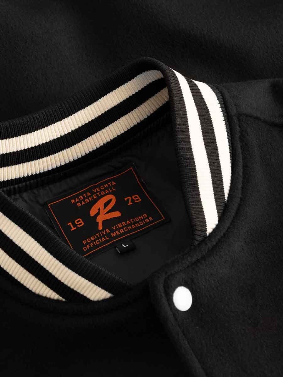 Schwarzer Baseballjacke mit weiß-schwarzem gestreiftem Rippstrick am Kragen, mit Label im Inneren, das "Rasta Vechta Basketball" und das Jahr 1979 zeigt.