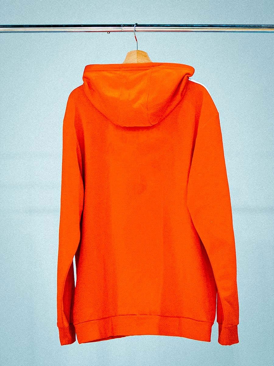 Ein orangefarbener Hoodie hängt an einem Holzkleiderbügel an einer Stange.