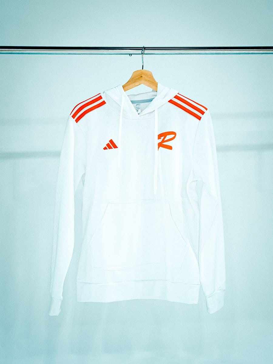 Weißer Hoodie mit roten Streifen auf den Schultern und rotem Logo auf der Brust, hängt an einem Holzkleiderbügel an einer Stange vor hellem Hintergrund.