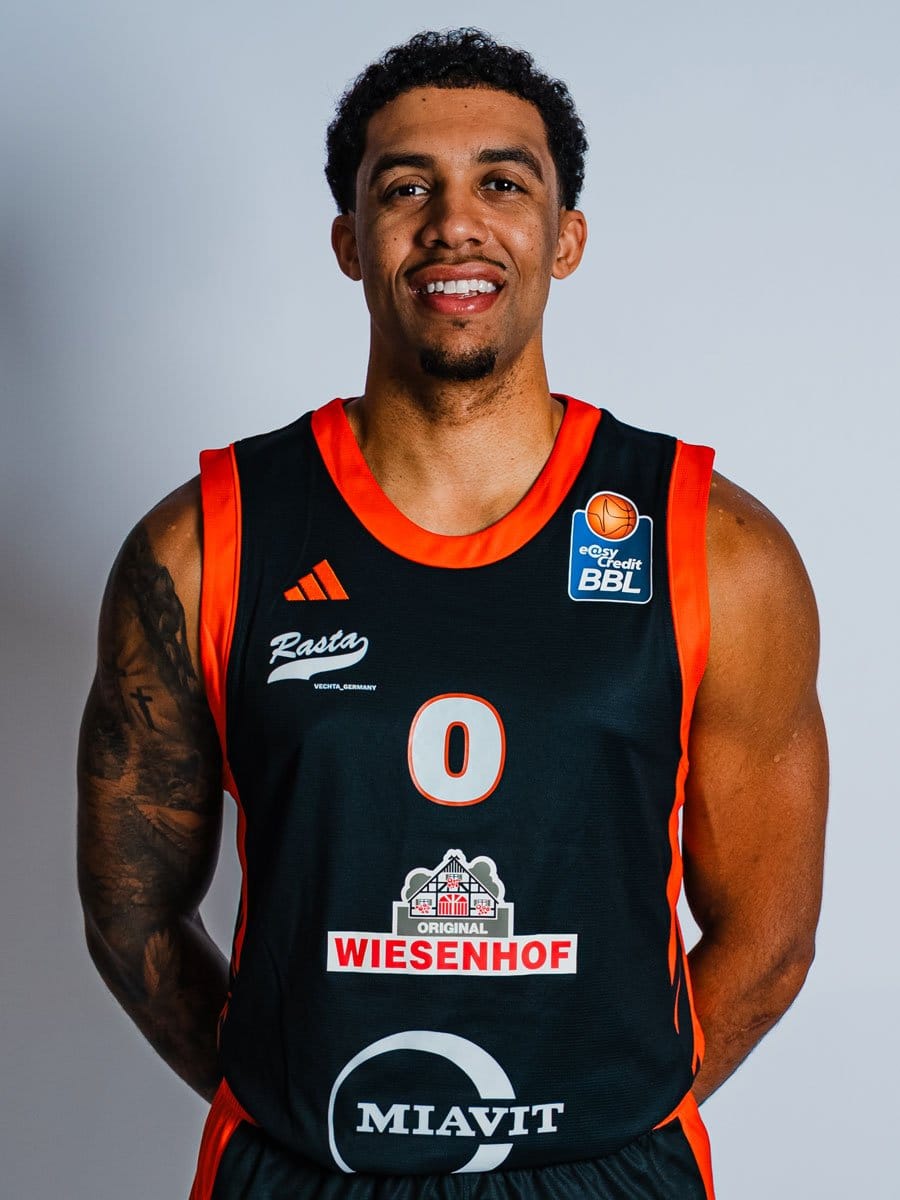 Junger männlicher Basketballspieler in schwarzem Trikot mit roten Akzenten, lächelnd, gegen hellgrauen Hintergrund.