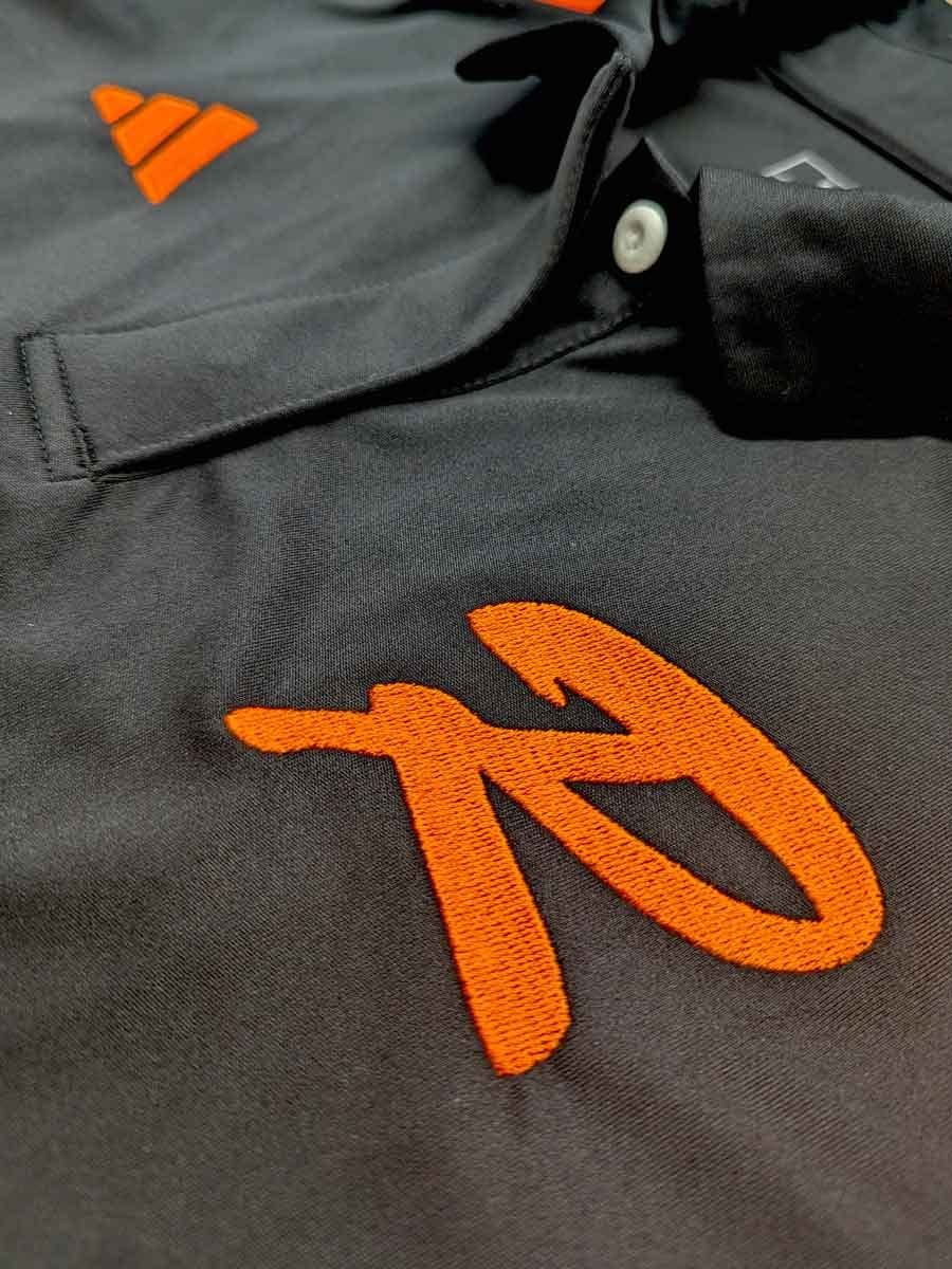 Schwarze Sporttasche mit orangefarbenem, gesticktem Logo und weißen Knöpfen am Reißverschluss.