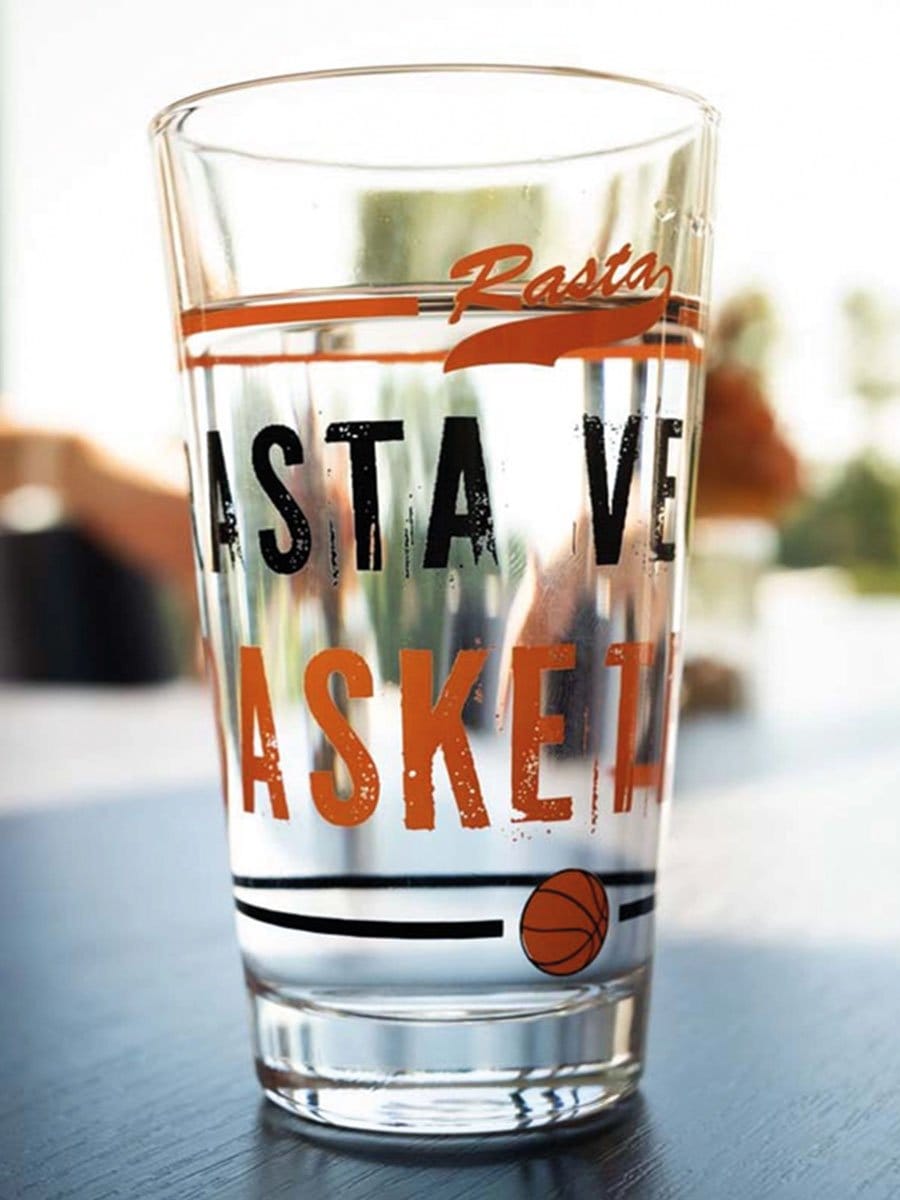 Ein transparentes Glas mit Wasser, auf dem der Schriftzug "Rasta" und "Save the Basket" in schwarzen und orangefarbenen Buchstaben sowie ein Basketball-Symbol zu sehen sind.