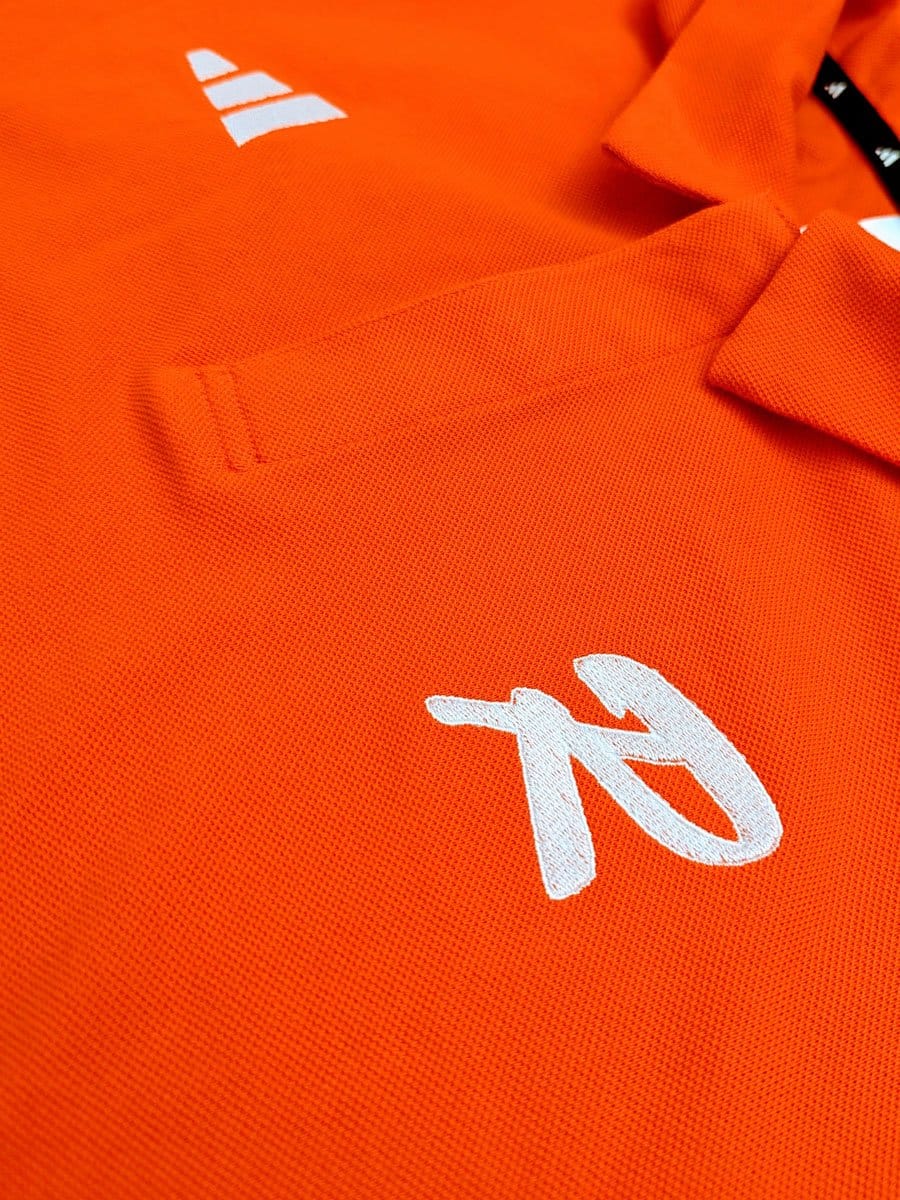 Nahaufnahme eines orangefarbenen Sportshirts mit weißem Logo und einer Tasche.