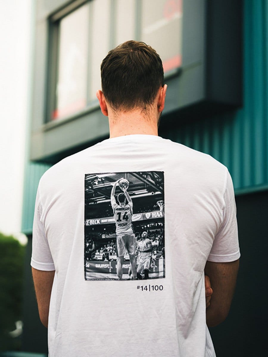 Rückansicht eines Mannes mit braunen Haaren, der ein weißes T-Shirt trägt. Auf dem T-Shirt ist ein schwarzes und weißes Basketballbild mit der Nummer 14 und der Angabe 100.