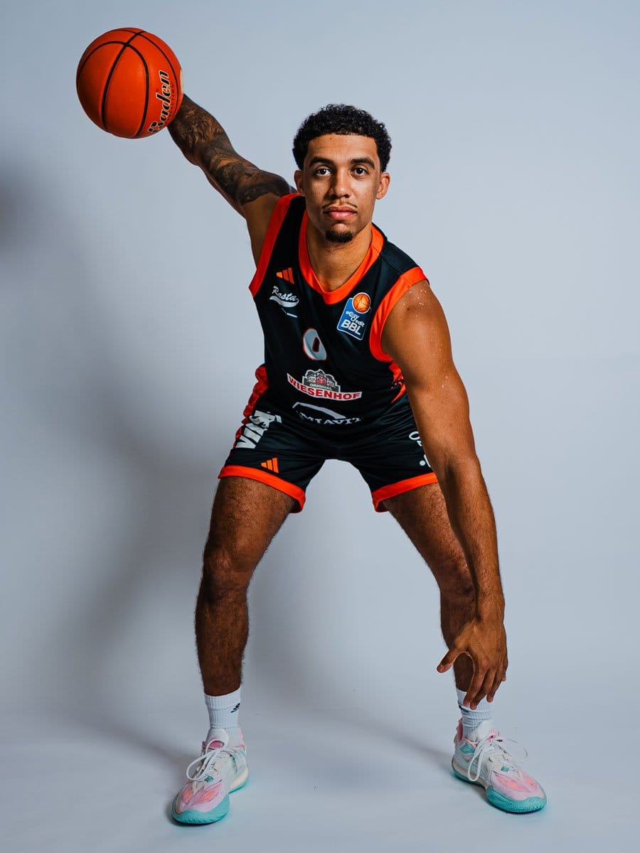 Ein junger männlicher Basketballspieler in einem schwarzen und roten Trikot, der einen Basketball hält und in einer sportlichen Haltung steht.