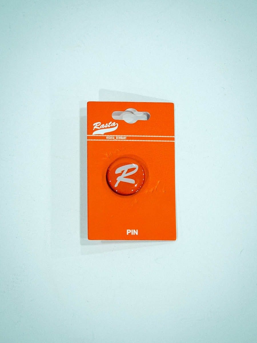 Roter PIN mit weißem Logo auf orangefarbenem Hintergrund in Originalverpackung.