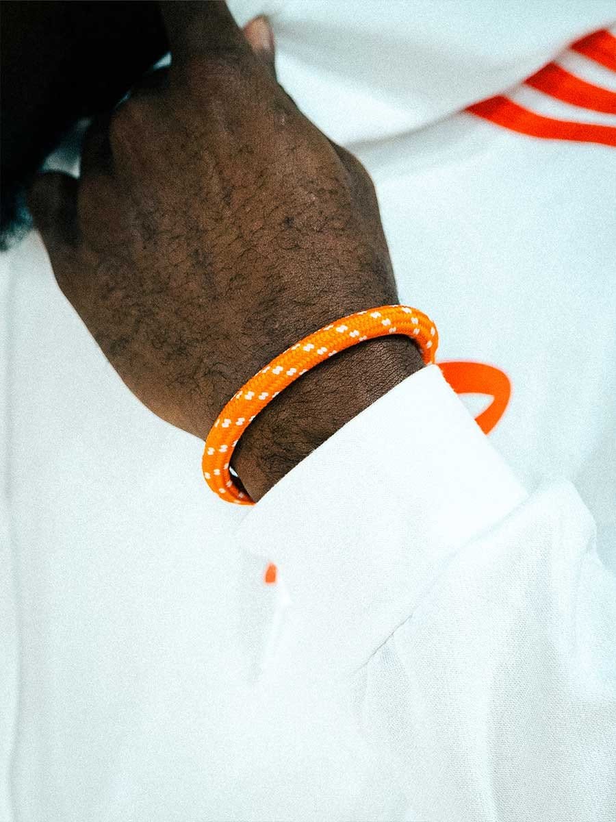 Hand mit dunkler Hautfarbe trägt einen orangefarbenen, reflektierenden Armband und eine weiße Kleidung mit orangefarbenen Akzenten.