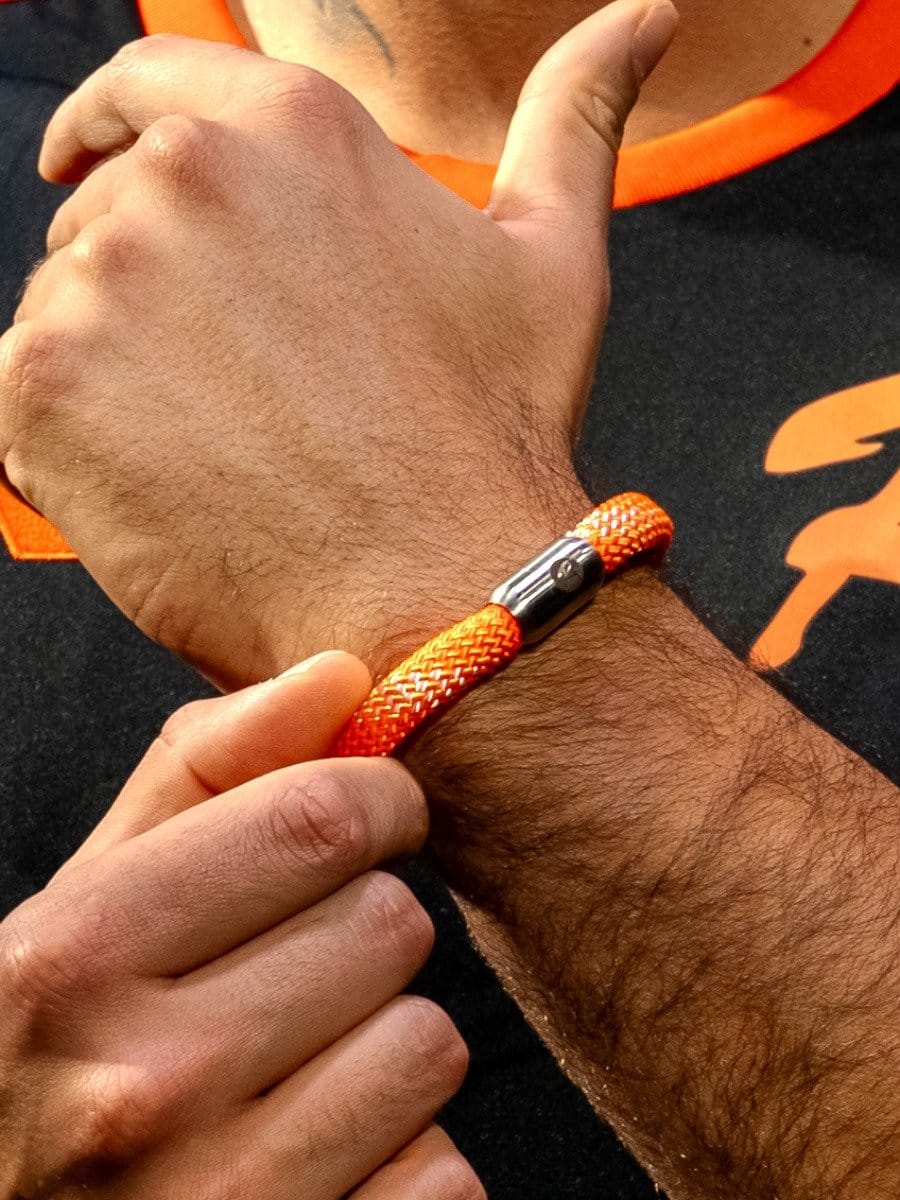 Hand mit einem orangefarbenen, geflochtenen Armband und einer silbernen Metallkappe, das an einem Handgelenk getragen wird.