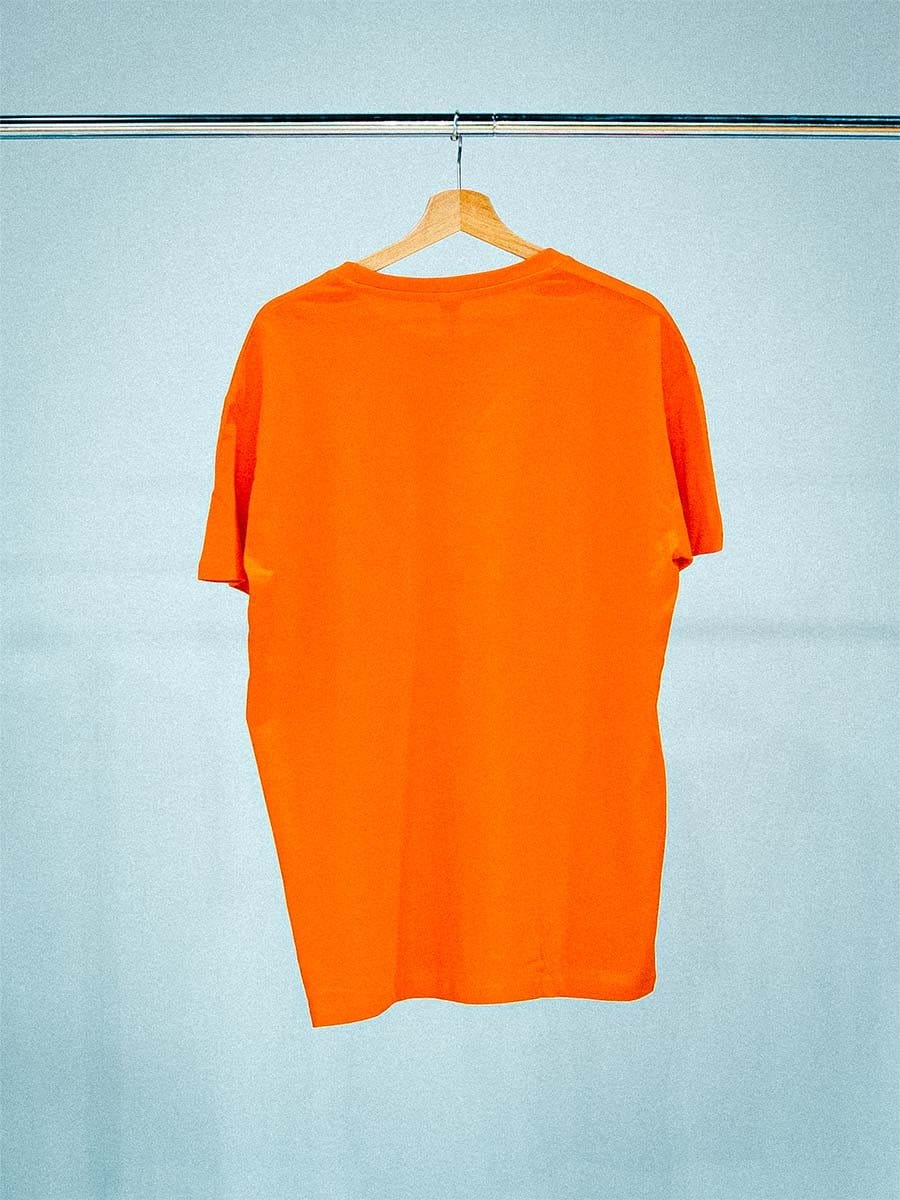 Ein orangefarbenes T-Shirt hängt an einem Holzkleiderbügel an einer Metallschiene vor einem hellblauen Hintergrund.