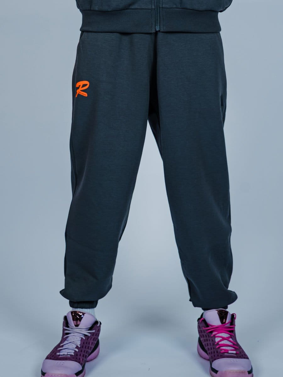 Dunkle Jogginghose mit elastischem Bund und einem orangefarbenen Logo an der Seite, kombiniert mit pinkfarbenen Sportschuhen.