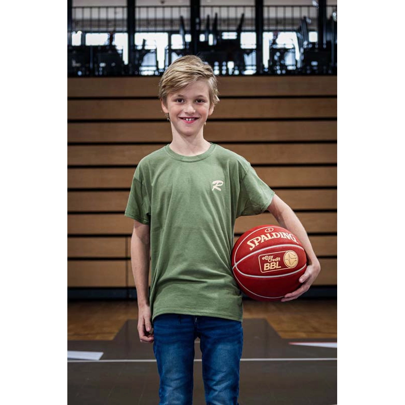 Kind von vorne mit Basketball in der Hand  im T-Shirt olivfarben mit Rasta Logo auf der Brust in weiß. 