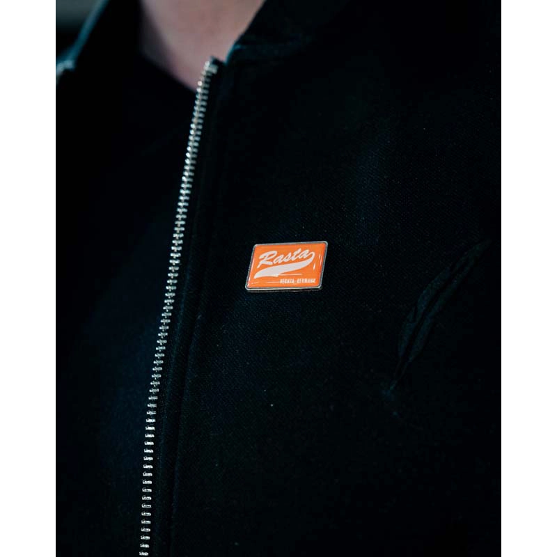 Schwarze Jacke mit Pin "RASTA" orange Frontansicht Rasta Vechta Germany Schriftzug in weiß.